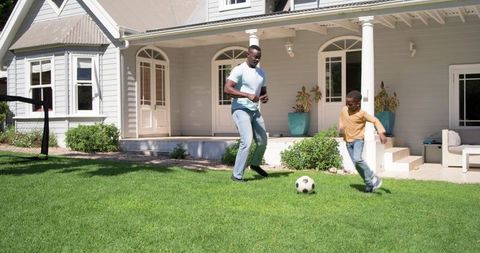 African american father and son playing soccer on suburban front lawn on sunny afternoon