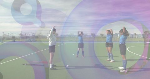 Female field hockey players stretching on turf pitch during team warmup and training