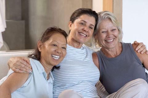 Three diverse mature women relaxing on sofa, sharing warm friendship and smiling together