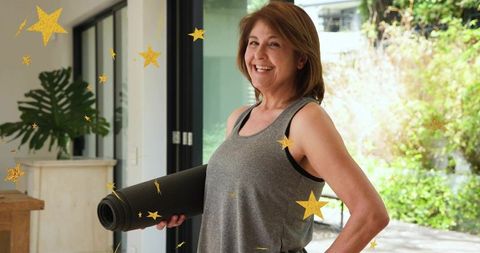 Senior woman holding yoga mat and smiling while preparing for home fitness routine