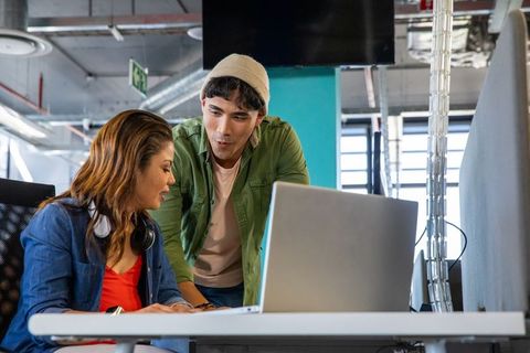 Young coworkers collaborating at modern open-plan office reviewing laptop and brainstorming