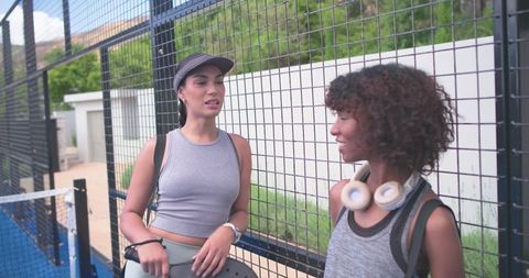 African american women chatting by paddle court with paddles and headphones