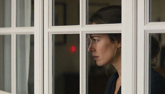 Woman gazing through window pane contemplative profile with red led glow