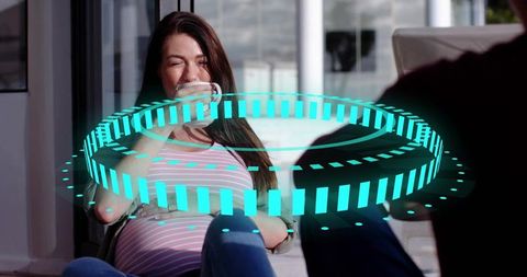 Pregnant woman relaxing on sunny terrace sipping coffee with futuristic teal hologram ring
