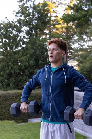 Man exercising with dumbbells in green garden