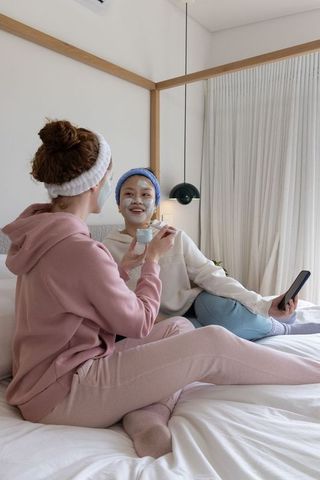 Friends sharing skincare night applying face masks and relaxing on cozy bed