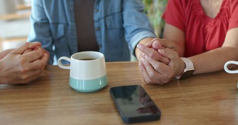 Women holding hands over coffee showing comfort and companionship in cozy kitchen