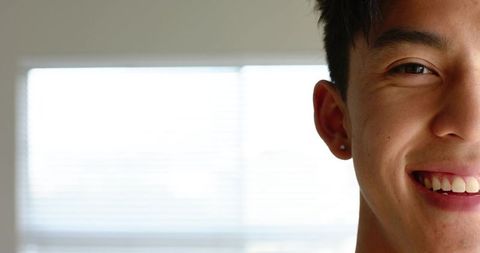Close-up asian man smiling at window with stud earring, high-key daylight portrait