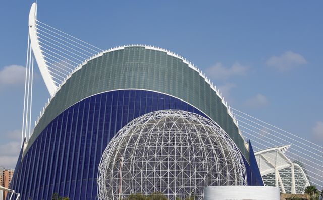 This image showcases the striking design of a modern architectural landmark in Valencia, Spain, against a clear blue sky. The futuristic building features hemispherical structures and a geometric dome. Useful for topics on modern architecture, travel destinations, engineering marvels, and Spanish culture.