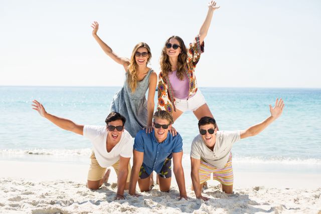 Cheerful friends forming pyramid with arms raised at beach on sunny day