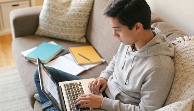 Teenager Studying on Sofa Using Laptop and Notebooks for Remote Learning and Homework