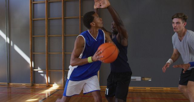 Teenagers engaged in an intense game of indoor basketball; one player preparing to shoot while being defended by another. Useful for illustrating teamwork, youth sports programs, active lifestyle promotions, and fitness training.