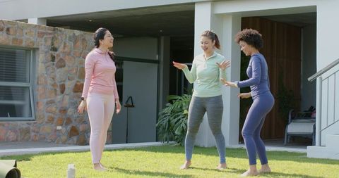 Three women stretching barefoot on home lawn before outdoor workout group warmup