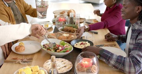 Diverse Friends Sharing Homemade Holiday Dinner Around Rustic Wooden Table, Cozy Gathering