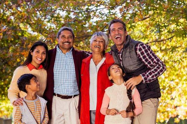Cheerful multi-generation family laughing while standing at park during autumn