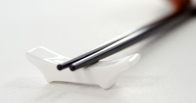 A pair of black chopsticks rests on a white chopstick holder, with copy space. The simplicity of the image emphasizes the elegance of Asian dining utensils.