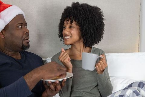 Cozy Christmas Morning Couple Sharing Breakfast in Bed, Woman Holding Mug, Man Wearing Santa Hat