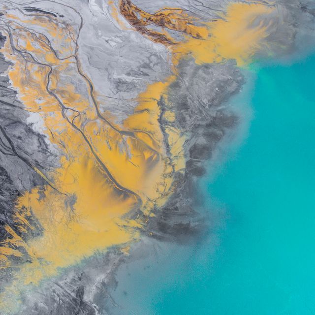 Aerial view of an abstract geothermal landscape featuring vibrant yellow sulfuric deposits contrasted with bright aqua blue waters. The image showcases natural patterns and colors, creating an eye-catching and unique visual. Ideal for use in environmental studies, promotional materials for travel and nature, backgrounds for artistic projects, or educational content on geology.