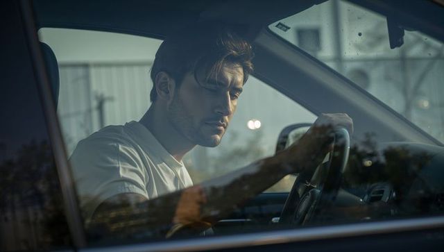 Brooding male driver sitting behind steering wheel gazing through rain-streaked car window