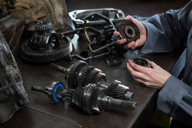 This image of a female mechanic examining car spare parts is ideal for illustrating concepts related to automotive repair, skilled trades, and mechanical engineering. Perfect for use in technical articles, advertisements for auto repair services, or educational materials highlighting the role of women in engineering and mechanical roles.