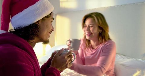 Couple sharing cozy morning coffee in festive bedroom with Santa hat and warm smiles