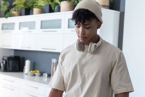 African american young man standing in modern kitchen wearing beanie and headphones