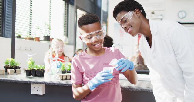 Young boy learning science experiment in classroom with guidance from teacher. Both wearing safety goggles and gloves. Can be used for educational content, STEM promotion, and school-related materials.