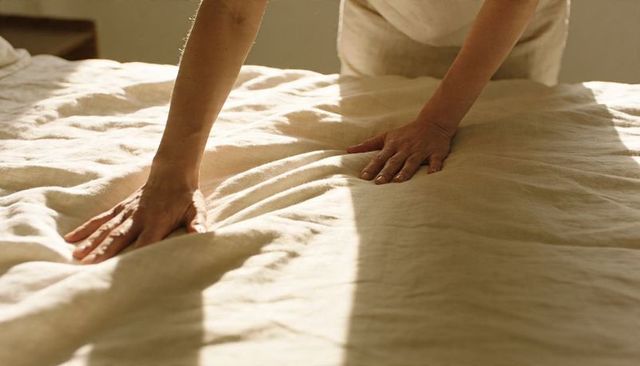 Smoothing linen bedding in sunlit bedroom hands pressing soft neutral duvet and sheets