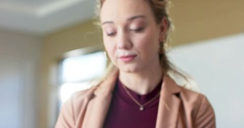 Thoughtful businesswoman looking down in warm office wearing tan blazer and gold jewelry