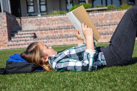 Teen girl relaxing on grass with book on sunny campus day