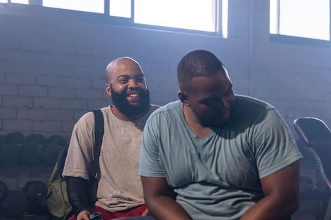 African american friends laughing and resting after workout on gym bench