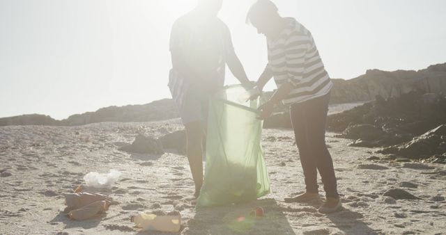 Backlit diverse senior couple collecting rubbish for recycling on sunny beach, copy space. Retirement, ecology, summer, vacations, volunteering and senior lifestyle, unaltered.