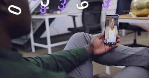 Holding smartphone watching live video call in casual open-plan office for remote teamwork
