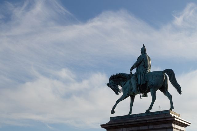 Historical equestrian statue framed against clear blue sky with scattered clouds. Ideal for articles on cultural heritage, public art, urban landmarks, and photography collections featuring iconic statues.