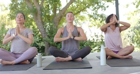 Women practicing meditation on shaded outdoor deck under trees for mindfulness and wellness