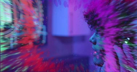 Curly musician holding headphones in neon studio, listening amid motion color burst