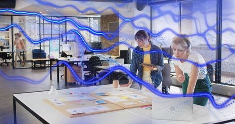 Creative team collaborating on moodboard and digital planning with blue data overlay in modern offic