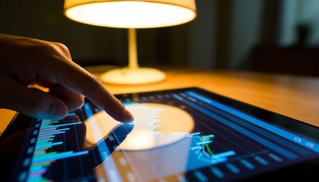 Tapping finger adjusting candlestick stock chart on tablet with warm desk lamp reflection