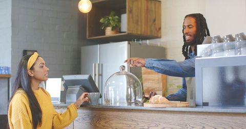 African american barista handing takeaway bag to indian woman at cozy cafe counter