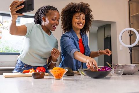 African American women filming colorful salad with smartphone and ring light for food blog