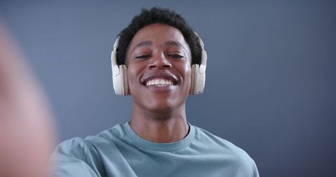 Young man wearing over-ear headphones smiling while taking selfie in minimalist studio