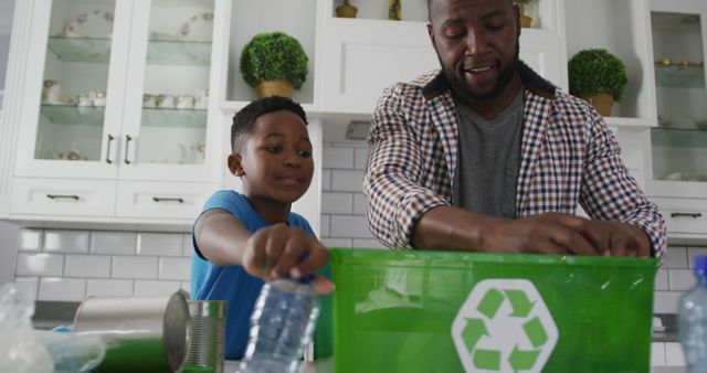 Happy african american father and son standing in kitchen putting plastic rubbish in recycling box. family spending time together at home.