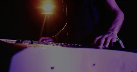 Silhouette of musician playing electronic keyboard in dim studio