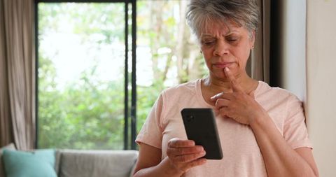 Senior Woman Contemplating with Smartphone near Window