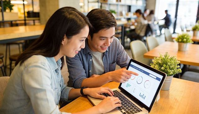 Young professionals collaborating and analyzing dashboard on laptop in cafe coworking space
