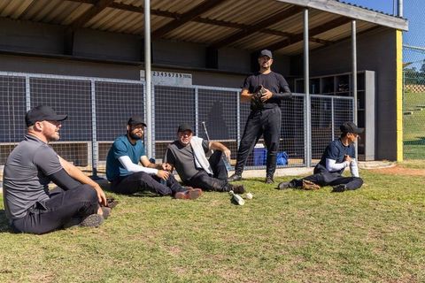 Baseball teammates resting at dugout talking strategy holding gloves and bats on sunny field