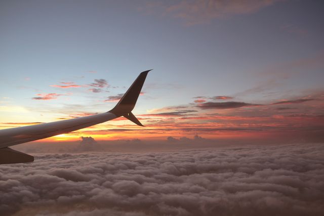 Ideal for travel promotions, aviation ads, and inspirational content. This image captures an airplane wing slicing through a breathtaking cloudscape with a stunning sunset, offering viewers a serene and exhilarating perspective.