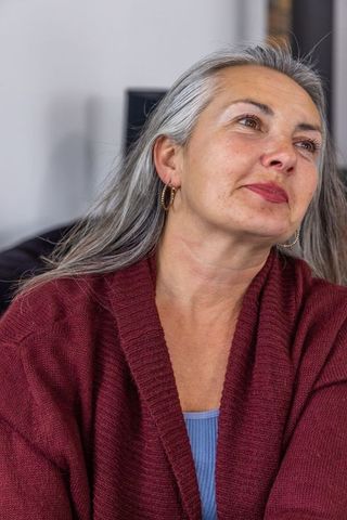 Mature woman in maroon cardigan and gold hoop earrings looking upward with serene gaze
