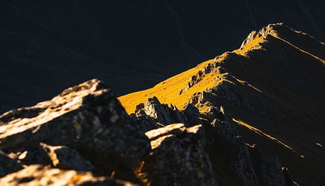 Sunlit alpine ridge at golden hour with dramatic rocky foreground and shadowed valley