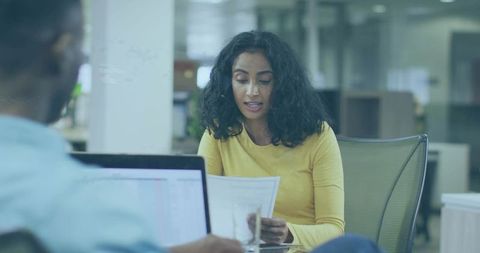Explaining woman in yellow top leading team discussion with papers in open-plan office